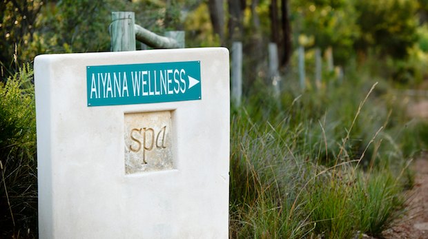 Handmade rendered wall with a sign pointing to Aiyana Wellness centre in front of a country path.
