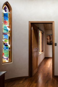 A wooden doorway leading to a bedroom with a stained glass window in the wall